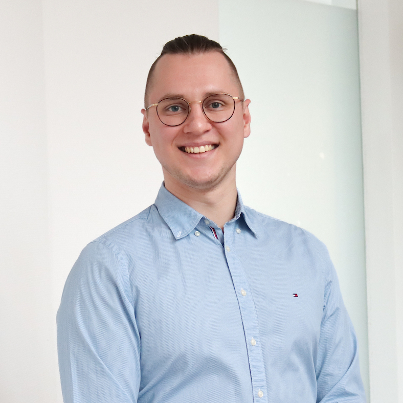 Ein Porträt von Alexander Kozyrev, er trägt ein blaues Hemd und eine runde Brille und lächelt fröhlich in die Kamera.