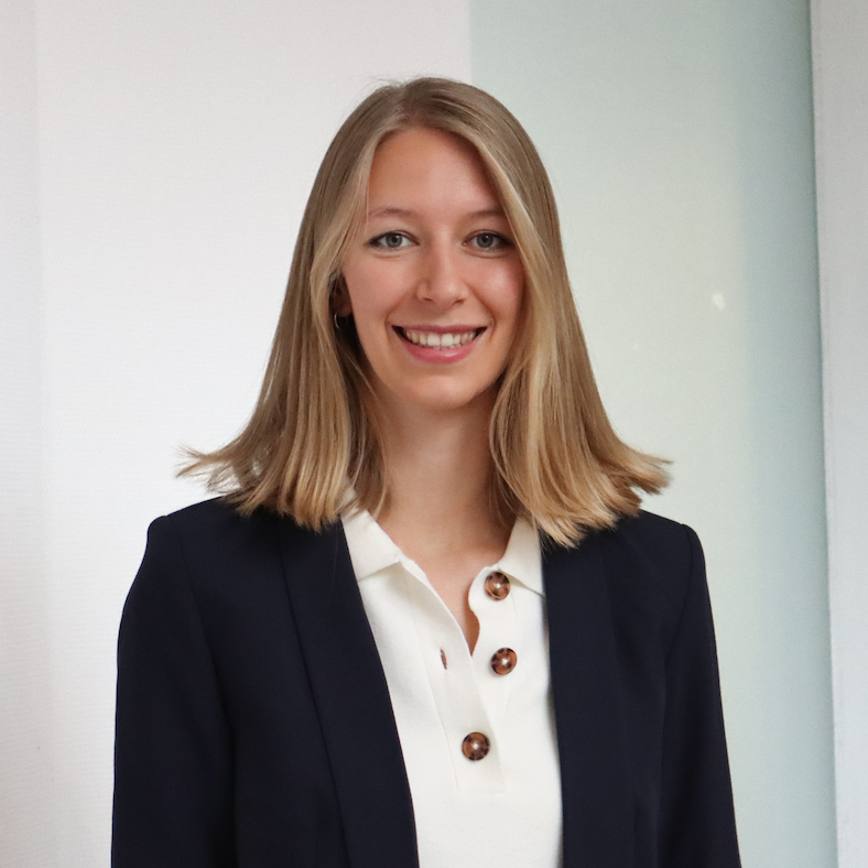 Ein Porträt von Marie Enzberger. Sie hat mittelblonde Haare und trägt einen dunkelblauen Blazer, darunter eine weiße Bluse. Sie lächelt fröhlich in die Kamera.