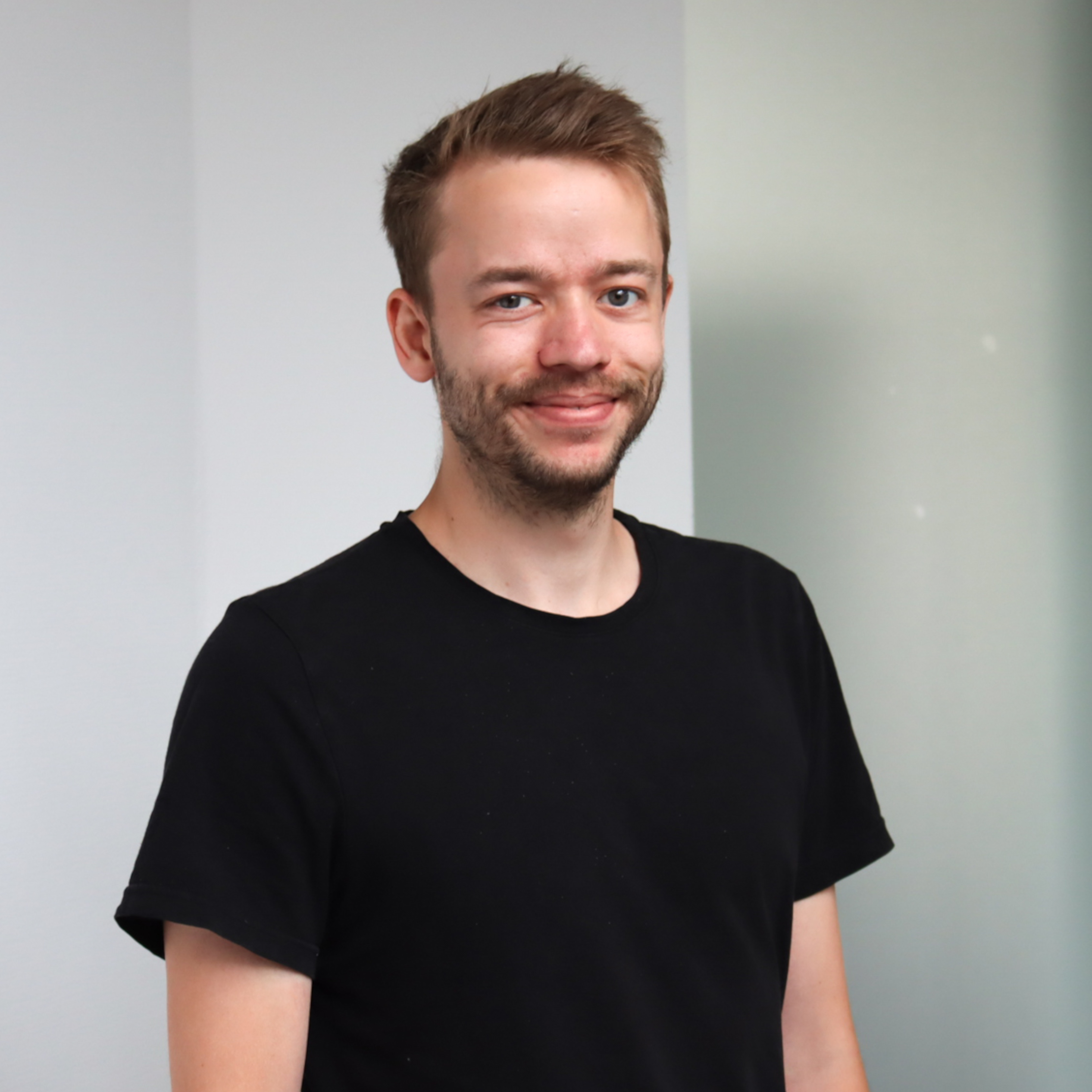 Ein Porträt von Julian Hessel. Er trägt ein schwarzes T-Shirt. Er lächelt fröhlich in die Kamera.